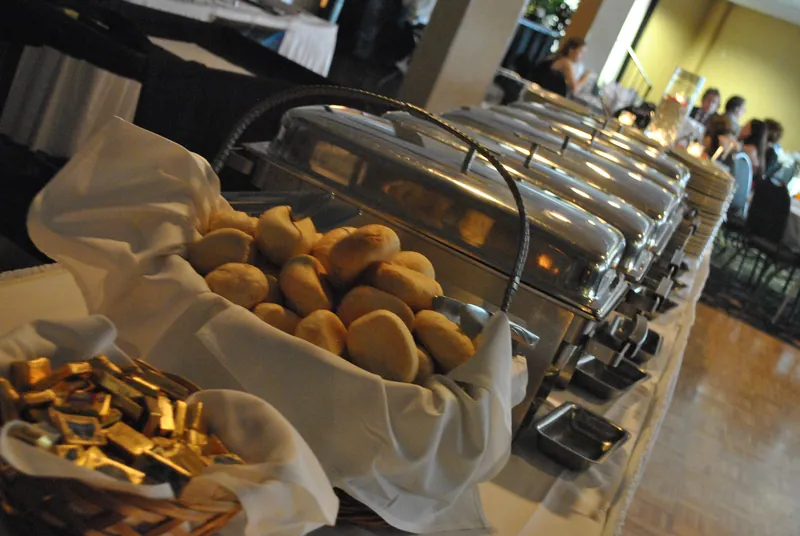 A bread basket stands beside a line of covered metal serving dishes on a long reception table.