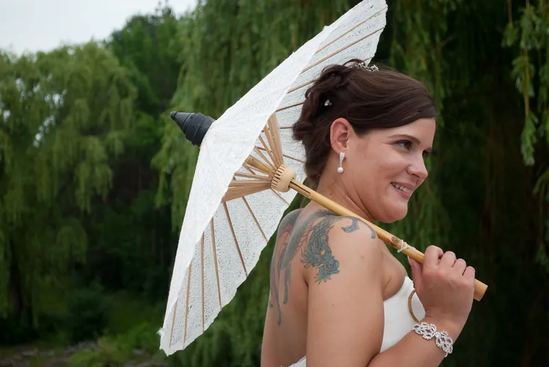 Angela looks over her shoulder while holding an ivory lace parasol above her shoulder outdoors.