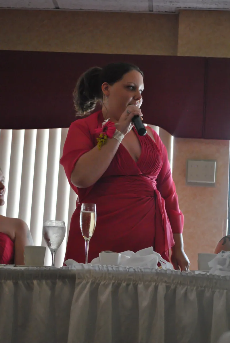 A speaker in a pink dress holds a microphone beside the reception table.