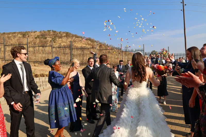 The couple walk between two lines of guests as confetti rises above the outdoor path.
