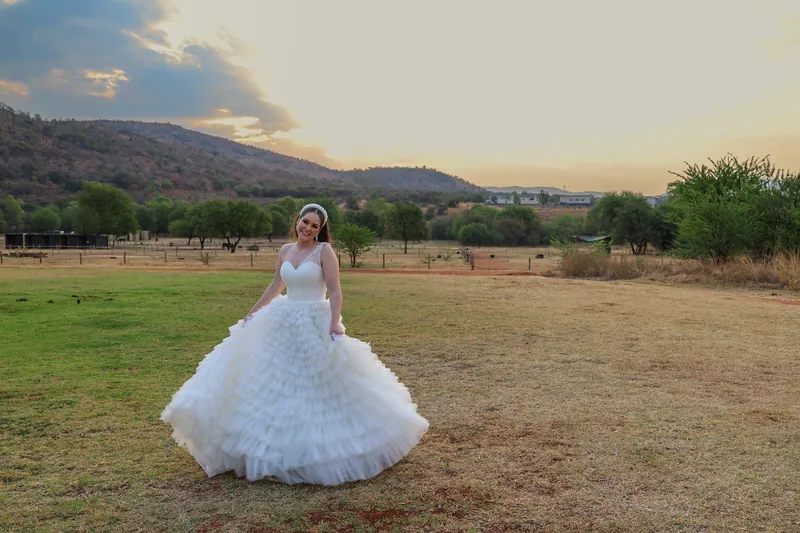 Roxy stands outdoors in an ivory gown with a fitted bodice and a full skirt of ruffled layers.