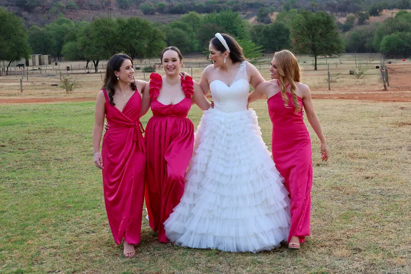 Roxy walks with three people in vivid pink dresses with different necklines and sleeves.
